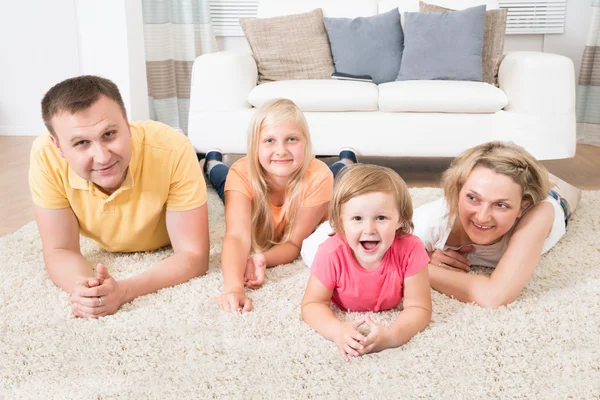 Familia joven feliz acostado en la alfombra — Foto de Stock