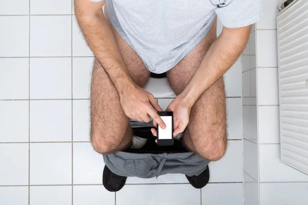 Uomo in toilette utilizzando il cellulare — Foto Stock