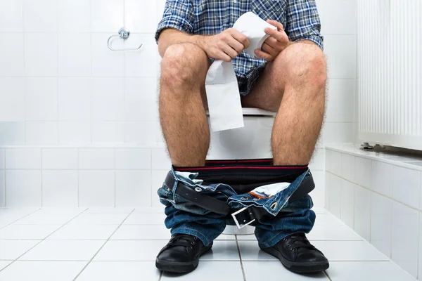Человек в туалете держит бумажный рулон — стоковое фото