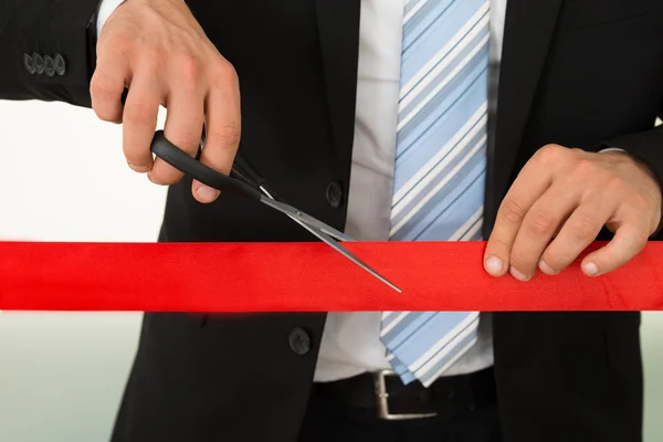 Бізнесмен різання червоною стрічкою ножицями — стокове фото