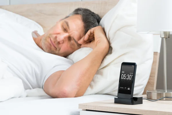 Человек на кровати с сотовым телефоном — стоковое фото