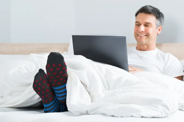 Uomo che utilizza il computer portatile nella sua camera da letto — Foto Stock