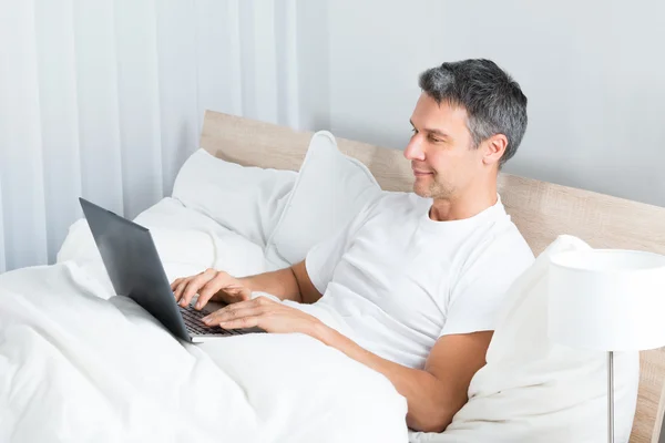 躺在床上使用笔记本电脑上的男人 — 图库照片