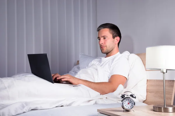 Άνθρωπος στο υπνοδωμάτιο χρησιμοποιώντας φορητό υπολογιστή — Φωτογραφία Αρχείου