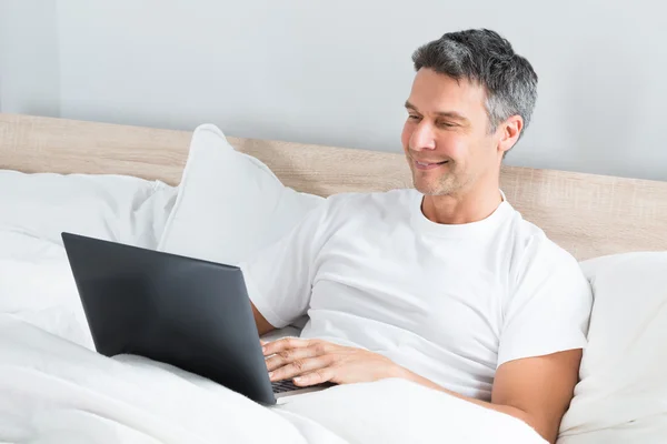 Hombre usando portátil en la cama — Foto de Stock