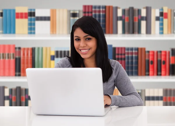 Mulher usando laptop na biblioteca — Fotografia de Stock