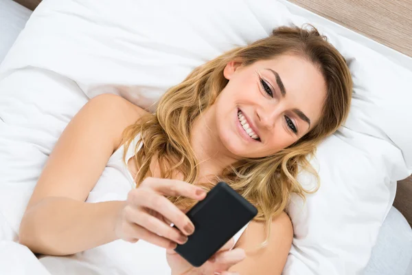 Kvinnan på sängen med hjälp av mobiltelefon — Stockfoto