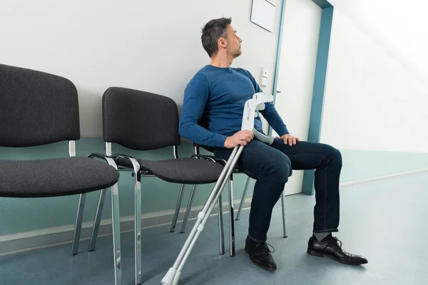 Man med kryckor sitter på stol — Stockfoto