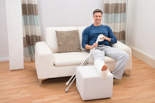 Человек, сидящий на диване с костылями — стоковое фото