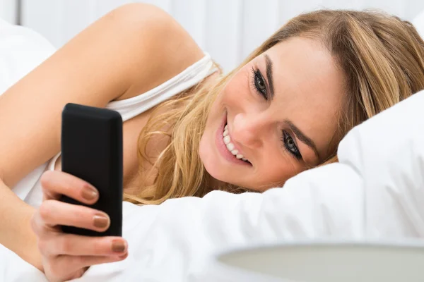 Frau mit Handy im Bett — Stockfoto