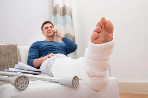 Человек со сломанной ногой и мобильником — стоковое фото