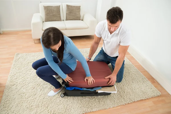 Pareja tratando de cerrar la maleta — Foto de Stock