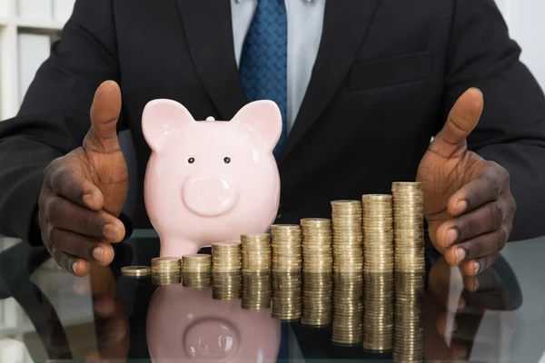 Бизнесмен со свиным банком и монетами — стоковое фото