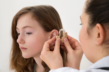 Doctor Inserting Hearing Aid In The Ear Of A Girl clipart