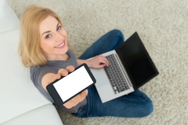 Mulher com telefone celular e laptop sentado no tapete — Fotografia de Stock