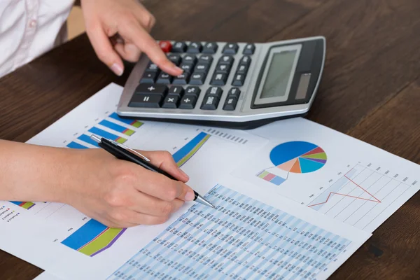 Бізнес-леді аналізуючи фінансовий звіт з калькулятором — стокове фото