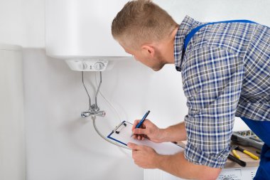 Plumber With Clipboard In Front Of Electric Boiler clipart