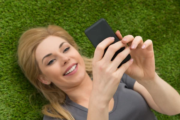 Mulher deitada na grama usando o telefone móvel — Fotografia de Stock