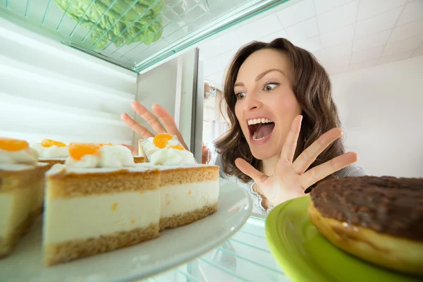 Frau schaut Kuchen im Kühlschrank an — Stockfoto