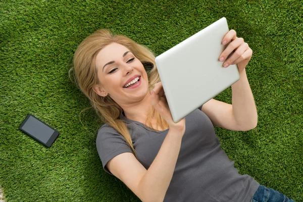 Mujer acostada sobre hierba usando tableta digital — Foto de Stock