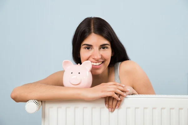 Mujer con Piggybank en el radiador en casa —  Fotos de Stock