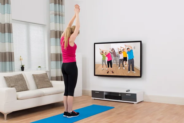 Vrouw kijken televisie en oefenen thuis — Stockfoto