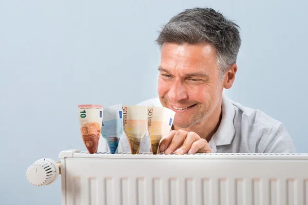 Homem colocando notas de euro no radiador — Fotografia de Stock