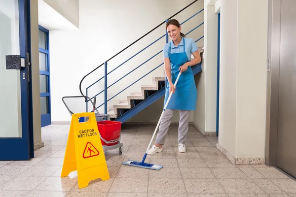 Trabajador con equipos de limpieza y letrero de piso húmedo — Foto de Stock