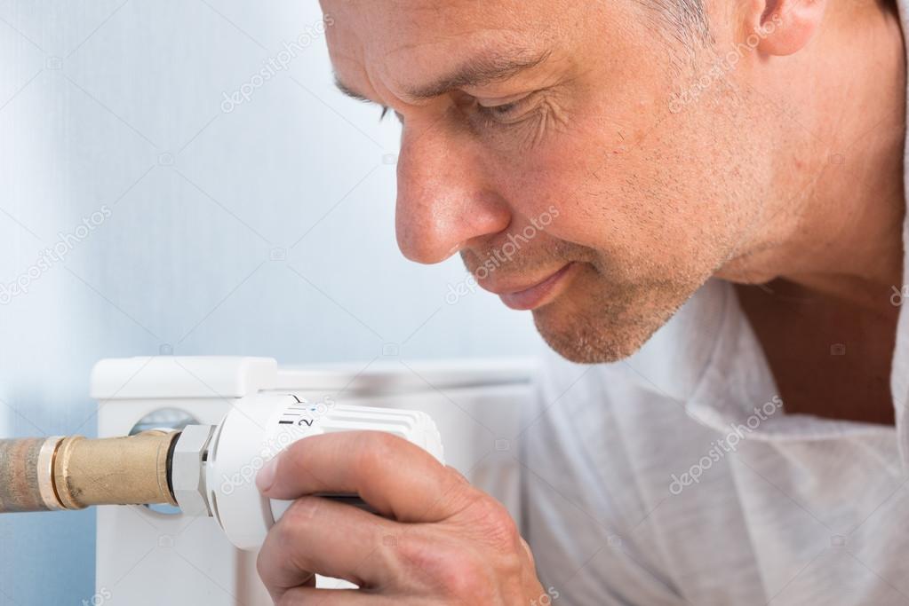 Man Adjusting Temperature Of Radiator Thermostat