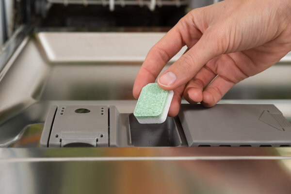 Hand Putting Dishwasher Tablet In Dishwasher Box