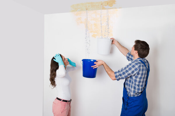 Женщина с рабочим собирает воду с потолка
