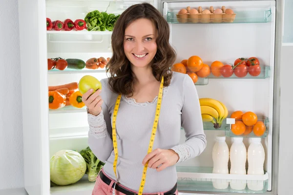 Mujer con cinta métrica y manzana cerca del refrigerador — Foto de Stock