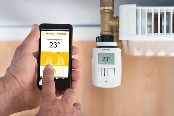 Hand aan te passen temperatuur van de thermostaat met behulp van mobiele telefoon — Stockfoto