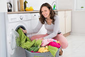 Egy nő ruhát tesz a mosógépbe.
