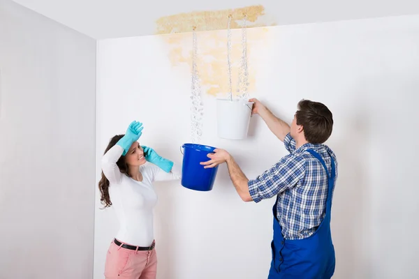 Frau mit Arbeiter sammelt Wasser von der Decke in Eimer — Stockfoto