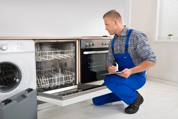 Handyman tittar på diskmaskin och skrivande — Stockfoto