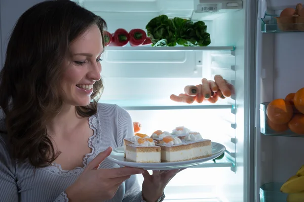 Mujer comiendo pastel cerca del refrigerador — Foto de Stock