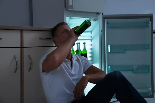 Человек сидит и пьет пиво на кухне — стоковое фото