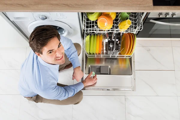 Человек кладет мыло в посудомоечную машину — стоковое фото