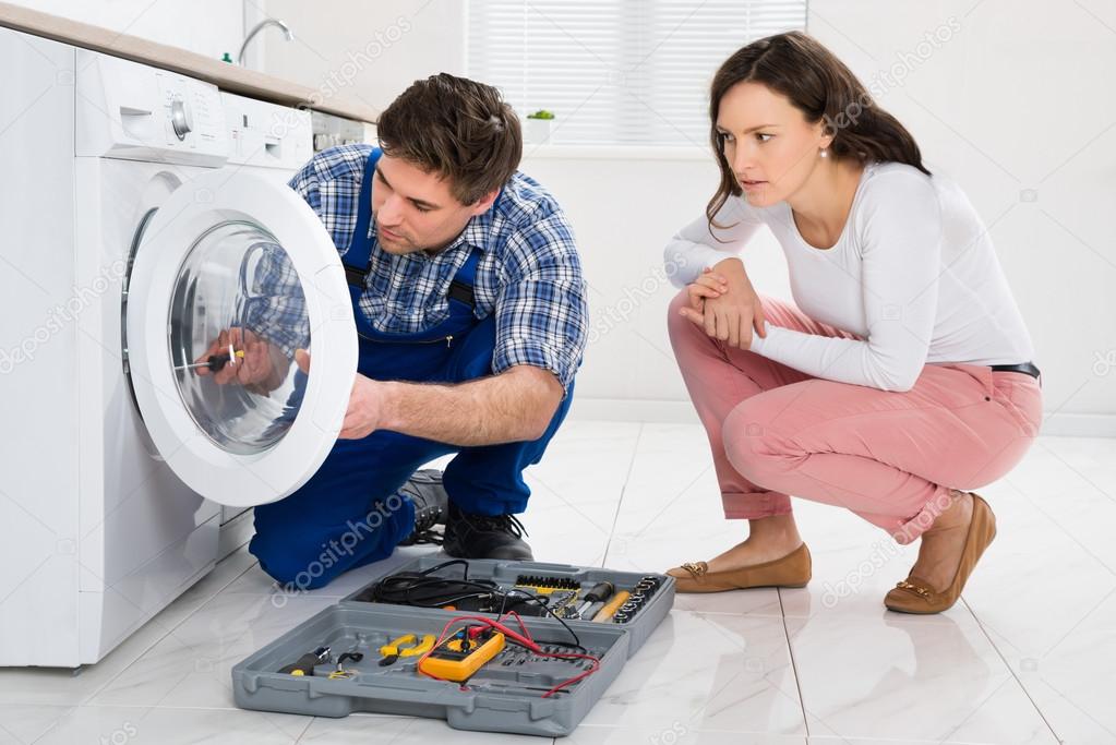 Repairman Repairing Washer In Front Of Woman