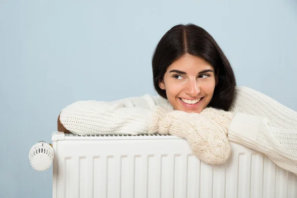 Kvinna i tröja lutar på Radiator — Stockfoto