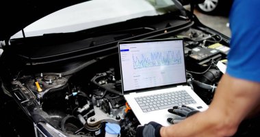 Kıdemli teknisyen garajda arabanın motorunu teşhis etmek için dizüstü bilgisayar kullanıyor.