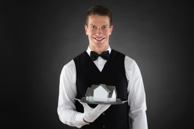 Tepsi minyatür bir ev tutarak garson