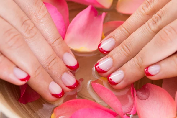 Donna mani in ciotola di acqua e petali — Foto Stock