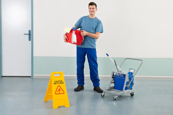 Работник с оборудованием для чистки и надписью "Осторожность на полу"
