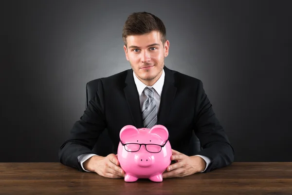 Geschäftsmann mit Sparschwein am Schreibtisch — Stockfoto