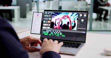 Videoları dizüstü bilgisayarda düzenlemek için mobil yazılım kullanan adam
