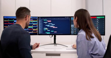 Ofis Proje Yöneticileri Bilgisayar Ekranında Gantt Grafiklerini Birlikte Analiz Ediyor.