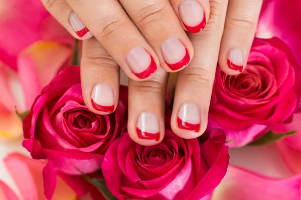 Handen met gemanicuurde nagel vernis geplaatst op rozen — Stockfoto