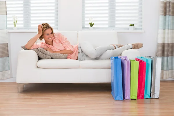 Mujer acostada en un sofá con bolsas de compras — Foto de Stock